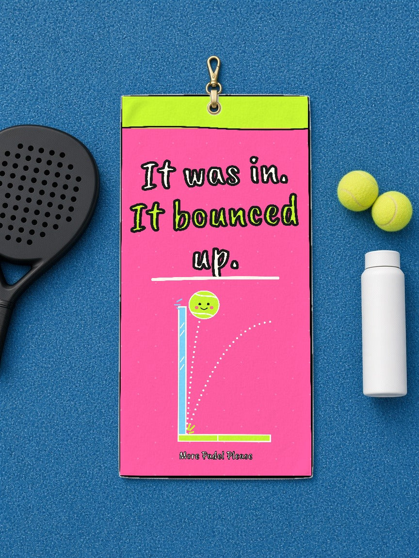 It Was In, It Bounced Up padel court towel laid flat on blue court turf with a padel racket, two balls and a water bottle